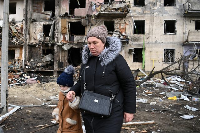 Žena s dítětem před panelovým domem na předměstí Kyjeva,  který byl zasažen ruským bombardováním  (25. února 2022) | foto: Profimedia
